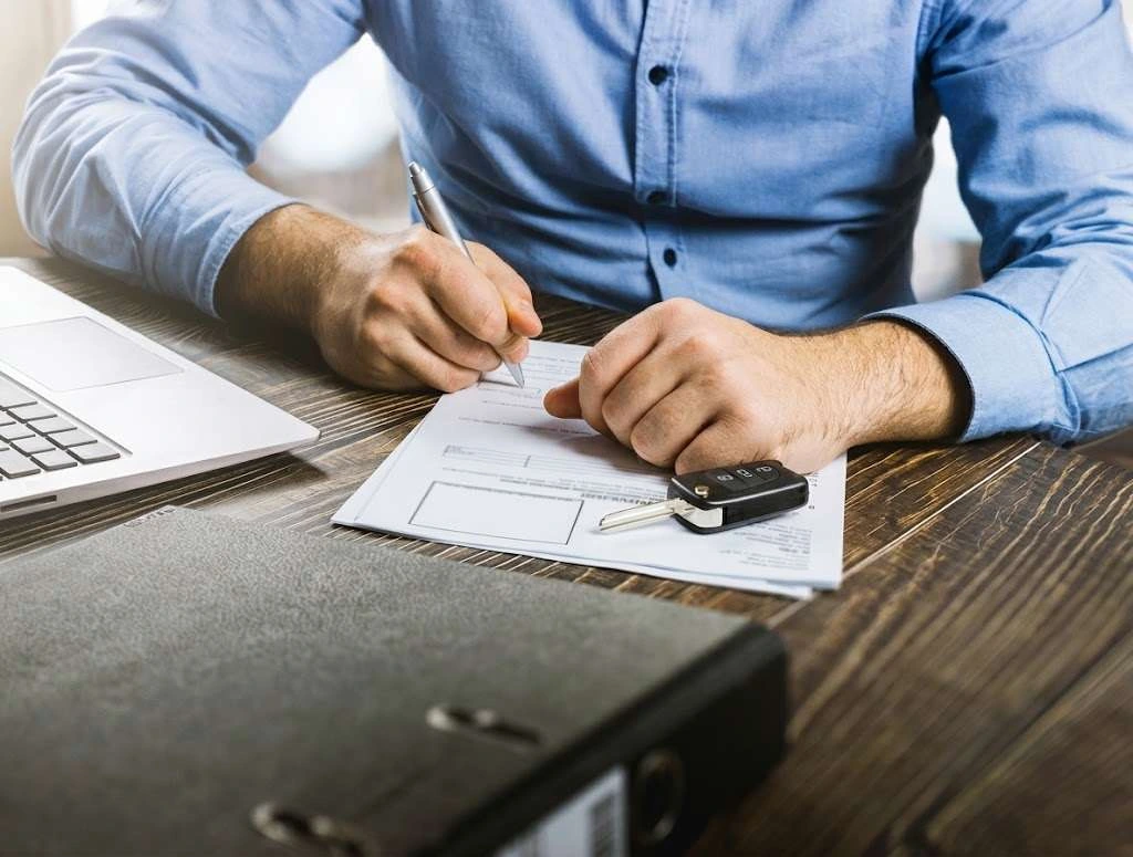 A dealer signing a purchase agreement with car keys on the desk