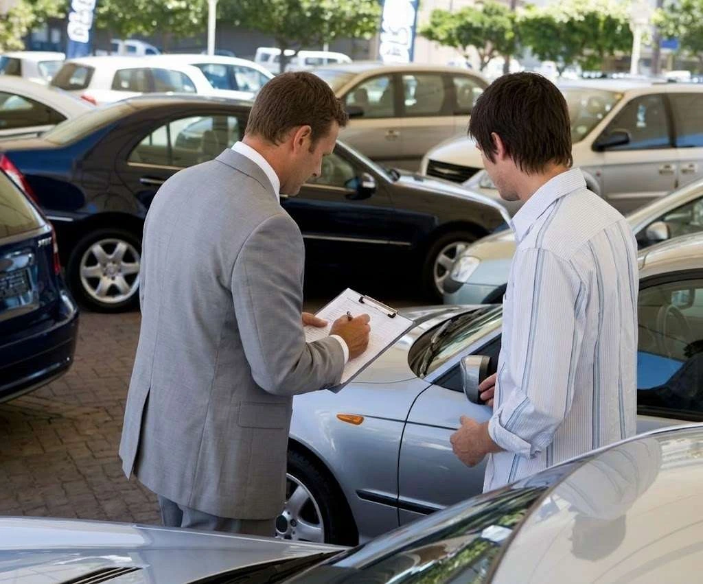 A used car buyer appraising a car on the lot with a clipboard